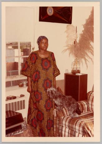 [Woman in red floral print dress in living room with small grey dog]
