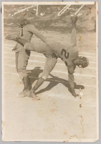 [Two young men in football uniforms and helmets, man in front doing a cartwheel]
