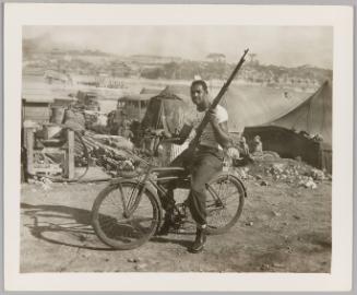 [Man sitting on bike with rifle in left hand]

