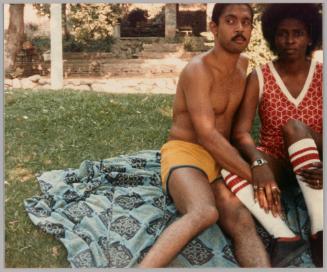 [Man in yellow shorts and woman in red and white sitting on a blanket]
