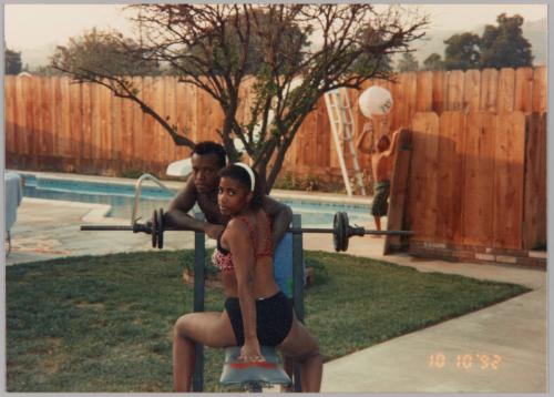 [Woman in swimsuit straddling workout bench, man leaning and boy playing with beach ball in background]
