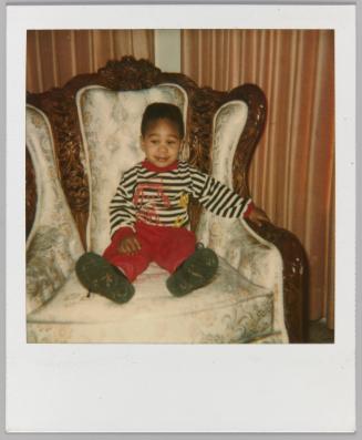 [Little boy in red pants sitting on  white armchair]
