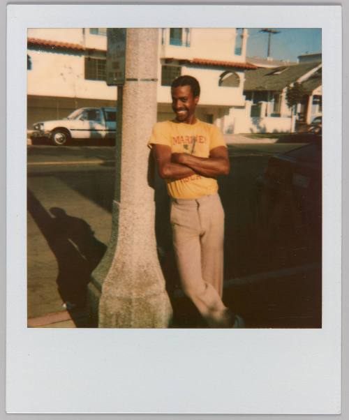 [Man smiling with arms crossed leaning against lamp post]
