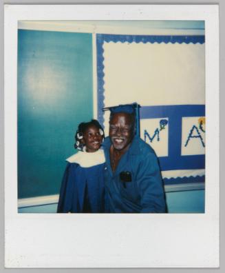 [Little girl in blue graduation gown posing with older man]
