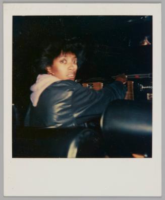 [Woman in black jacket with light-coloured hood popping out from underneath, she is turning back to look at the camera]