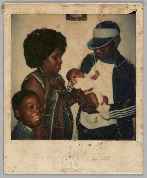 Dec 19 [Man in visor and blue track jacket holding squirming baby, to the left there is a boy laughing and a woman looking down at the baby]