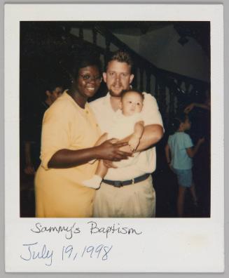 Sammy's Baptism July 19, 1998 [Woman in yellow outfit standing beside man holding a baby]