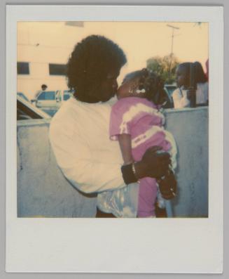 [Man in white sweatshirt holding a girl and giving her a kiss, she is wearing a pink and white outfit, they are outside]