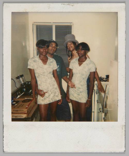 [Two teenage girls in matching short-sleeved dresses standing in front of two teenage boys, boy on right in top hat]