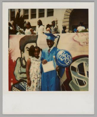 [Boy in blue cap and gown holding a balloon that reads "Class of '97," girl in floral pattern dress standing beside him]