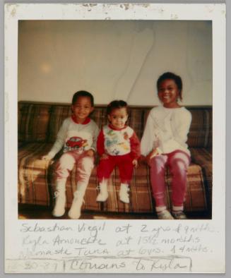 Sebastian Virgil at 2 yrs & 9 mths. Kyla Amonette at 15 1/2 months Namaste Tara at 6 yrs & 4 mths. [12-30?]-87 Cousins to Kisla [Three children sitting on brown plaid couch]