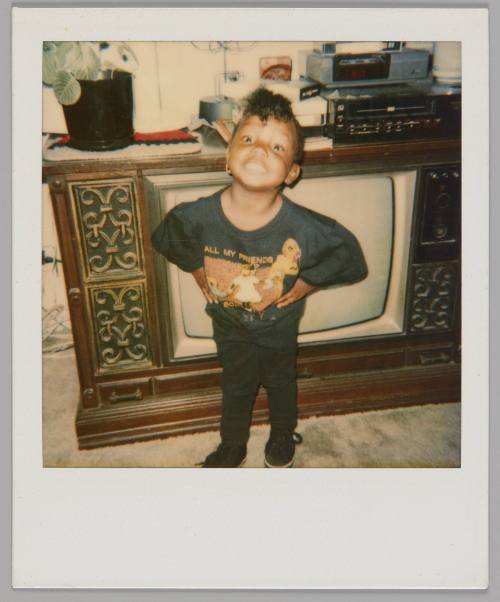 [Girl posing with her hands on her hips and a big smile, she is standing in front of a television set and is wearing a black shirt that reads "All my friends..."]