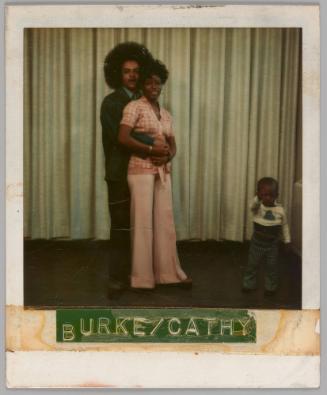 Burke/Cathy [Man holding woman in pink outfit from behind with a young child to the right, curtain behind them]