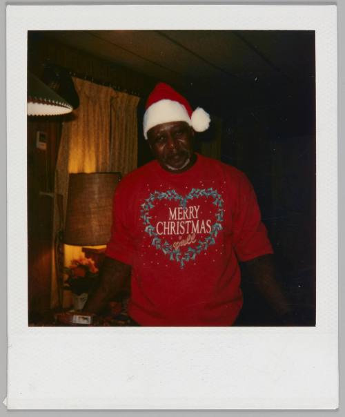[Man in Santa Claus hat and red sweater with a heart-shaped wreath and the words "Merry Christmas y'all"]