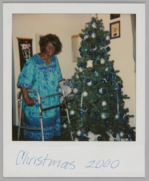 Christmas 2000 [Woman in blue embroidered dress standing with walker by a Christmas tree with silver ornaments]