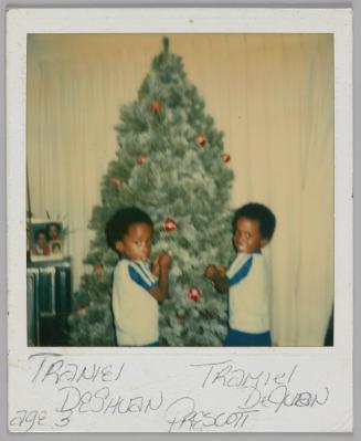 Traniel DeShaun Tramiel DeJuan Prescott age 3 [Two boys in matching blue and grey t-shirts putting ornaments on a Christmas tree]