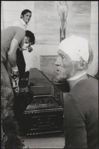 A man with a head injury stands by as two men prepare a coffin for burial in the Osoppo cemetery after the Friuli earthquake in 1976