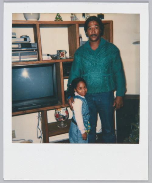 [Man in green sweater standing with man around little girl's shoulder]