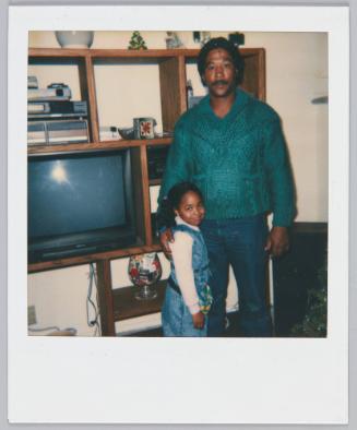 [Man in green sweater standing with man around little girl's shoulder]
