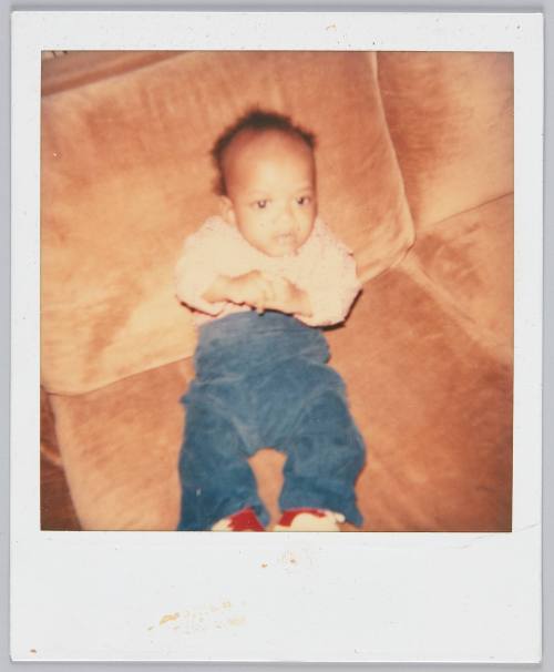 [Infant propped up on couch wearing blue pants and plaid shirt]