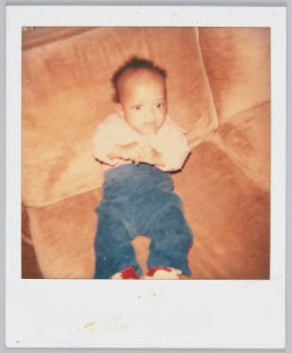 [Infant propped up on couch wearing blue pants and plaid shirt]