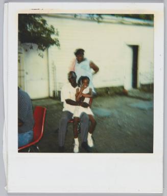 [Man wearing sunglasses sitting on red chair with little girl sitting on his lap]