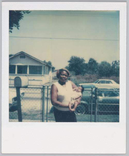 [Woman holding infant outside of house]