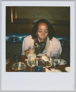 [Woman with pink cardigan blowing out candle on slice of cake]