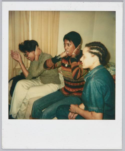 [Three young women sitting on bed, woman on far right has cornrows]