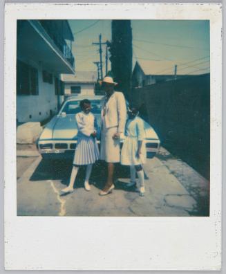 [Woman and two young girls posing in their formal outfits in front of car]