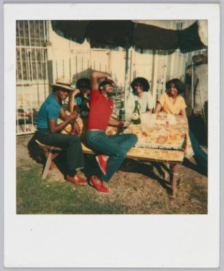 [Stylish group sitting around picnic table, young man in the front wears red tshirt and matching shoes]