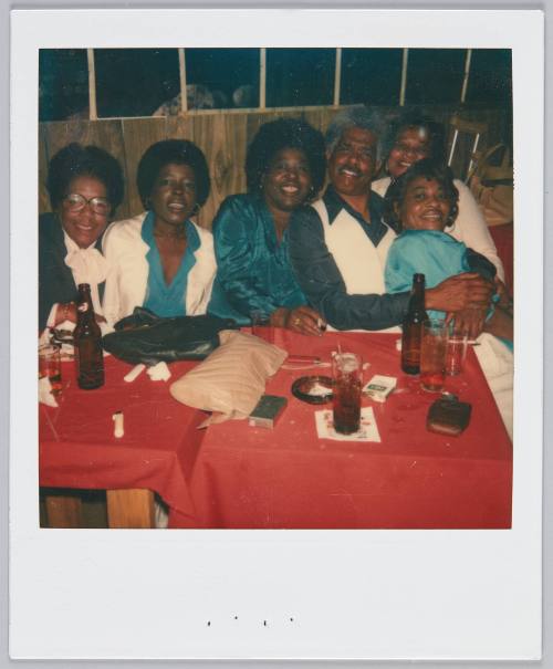 [Group of six gathered on one side of table covered in red tablecloth]