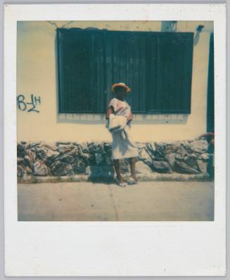 [Woman in pencil skirt and pink hat posing in front of side of building]