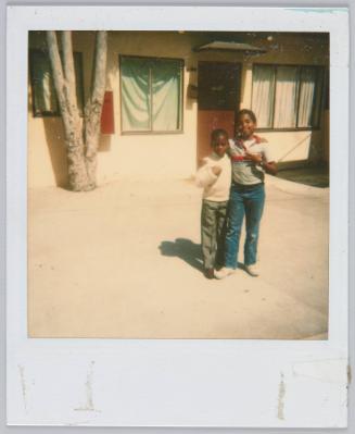 [Two young boys with they arm around each other posing in front of home]