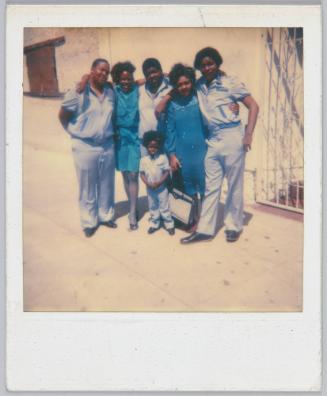 [Family gathered with arms around each other on sidewalk]