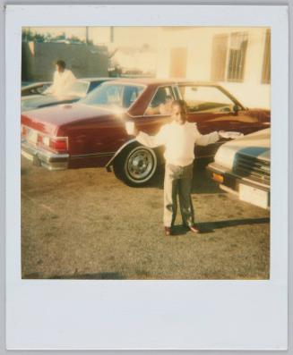 [Boy in dress pants standing in parking lot holding up a plate and cup]