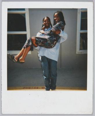 [Young couple grinning, while young man holds up young woman in his arms]