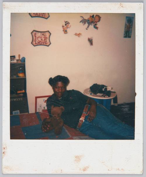 [Girl laying on bed next to brown teddy bear]