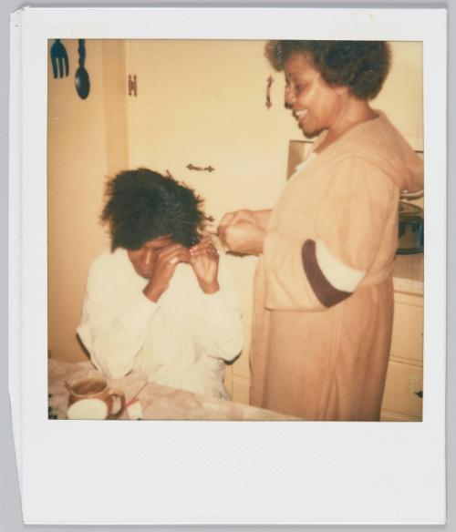 [Woman doing young woman's hair as she sits at kitchen table]