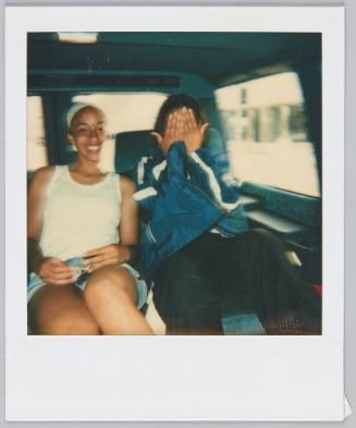 [Two adolescents in backseat of car, teen on right covering their face]