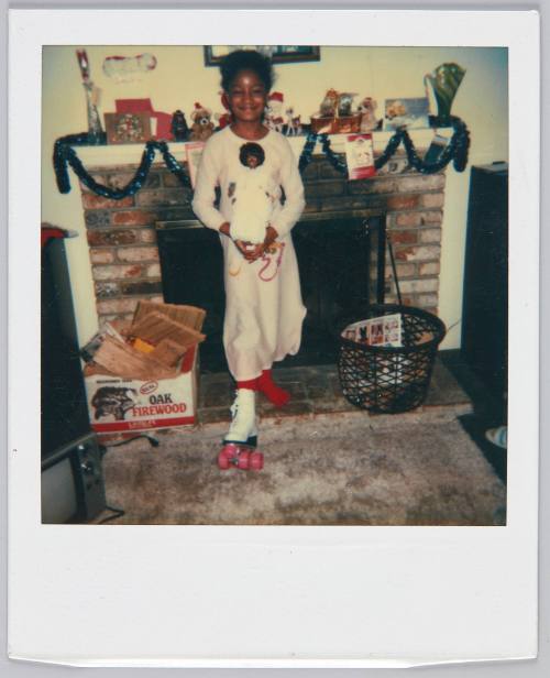 [Little girl holding doll and smiling with a rollerskate on her right foot]