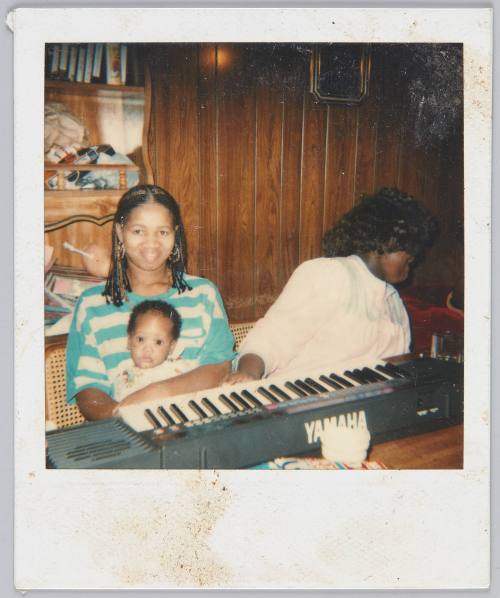 [Two woman sitting in front of YAMAHA keyboard, woman on left holding infant on her lap]