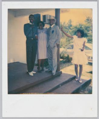 [Group of three standing on stoop, girl in white dress and stockings standing two steps lower than group]
