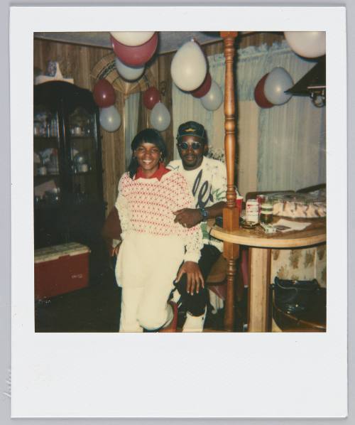 [Woman in red and white patterened sweater standing in between man's legs smilling]