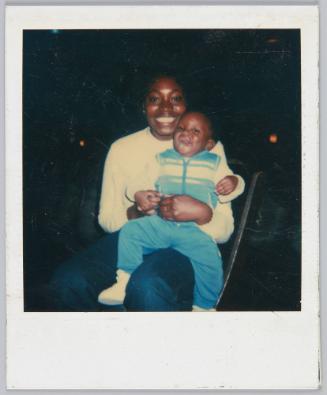 [Young woman smiling and holding toddler on her knee]