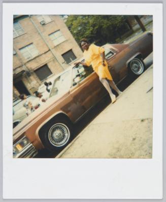 [Woman in yellow dress and white stockings posing next to brown car]