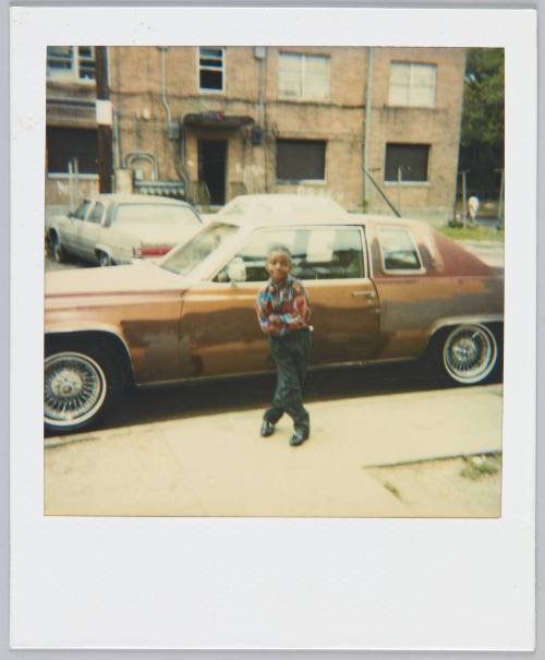 [Little boy in plaid shirt posing in front of brown car]