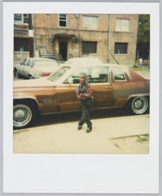 [Little boy in plaid shirt posing in front of brown car]