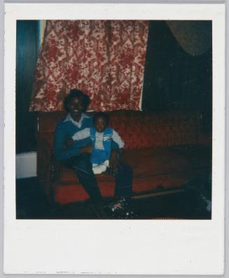 [Young woman sitting on red velvet couch with toddler boy sitting on her lap]