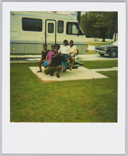[Family gathering on picnic chair, RV parked behind them]